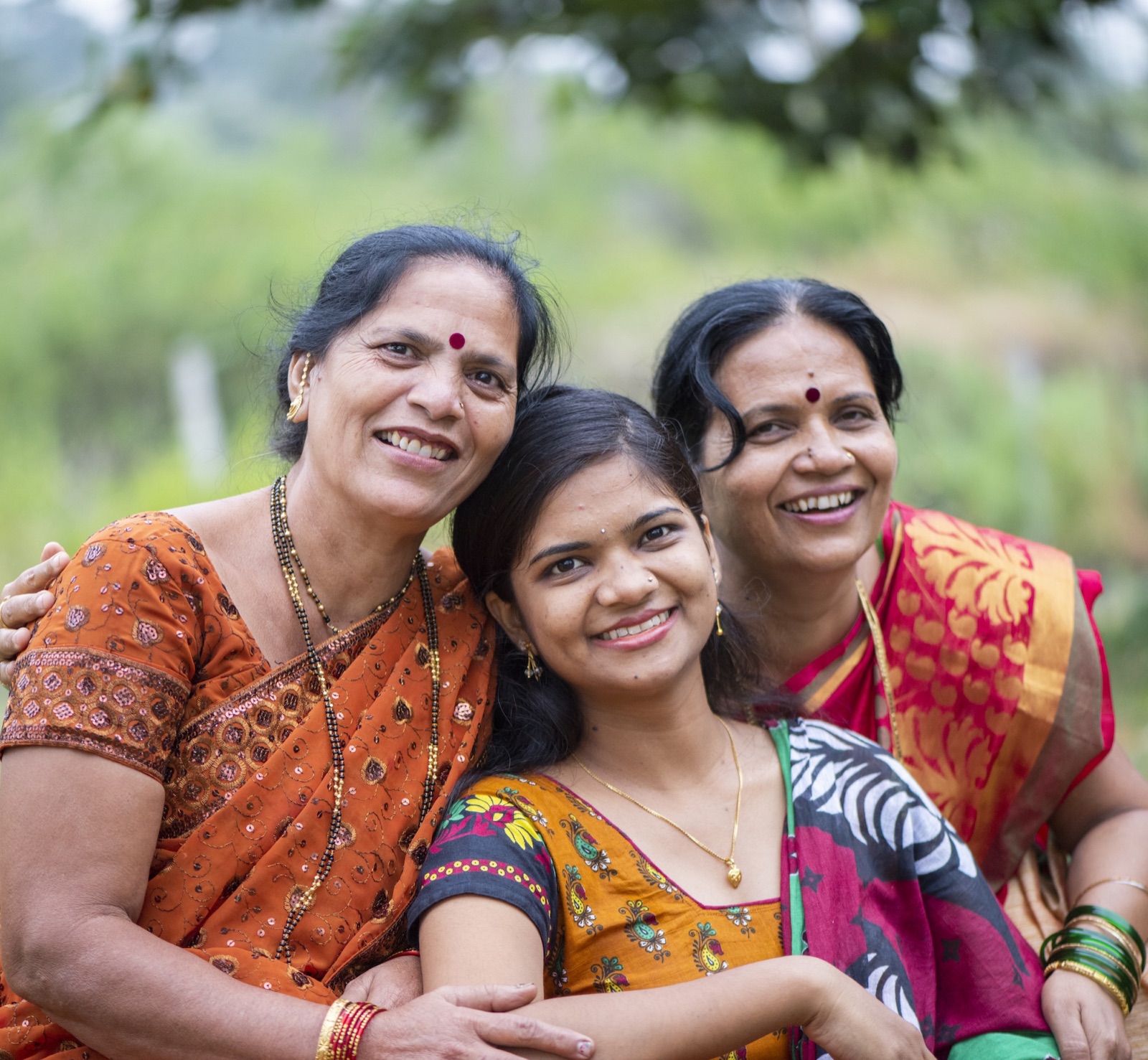 Three generations of Indian women in saris, smiling together outdoors